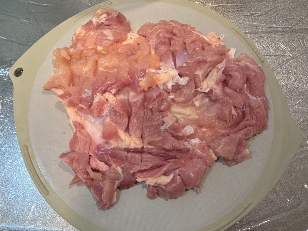 切れ目を入れて広げた鶏もも肉。まな板の下にはラップ